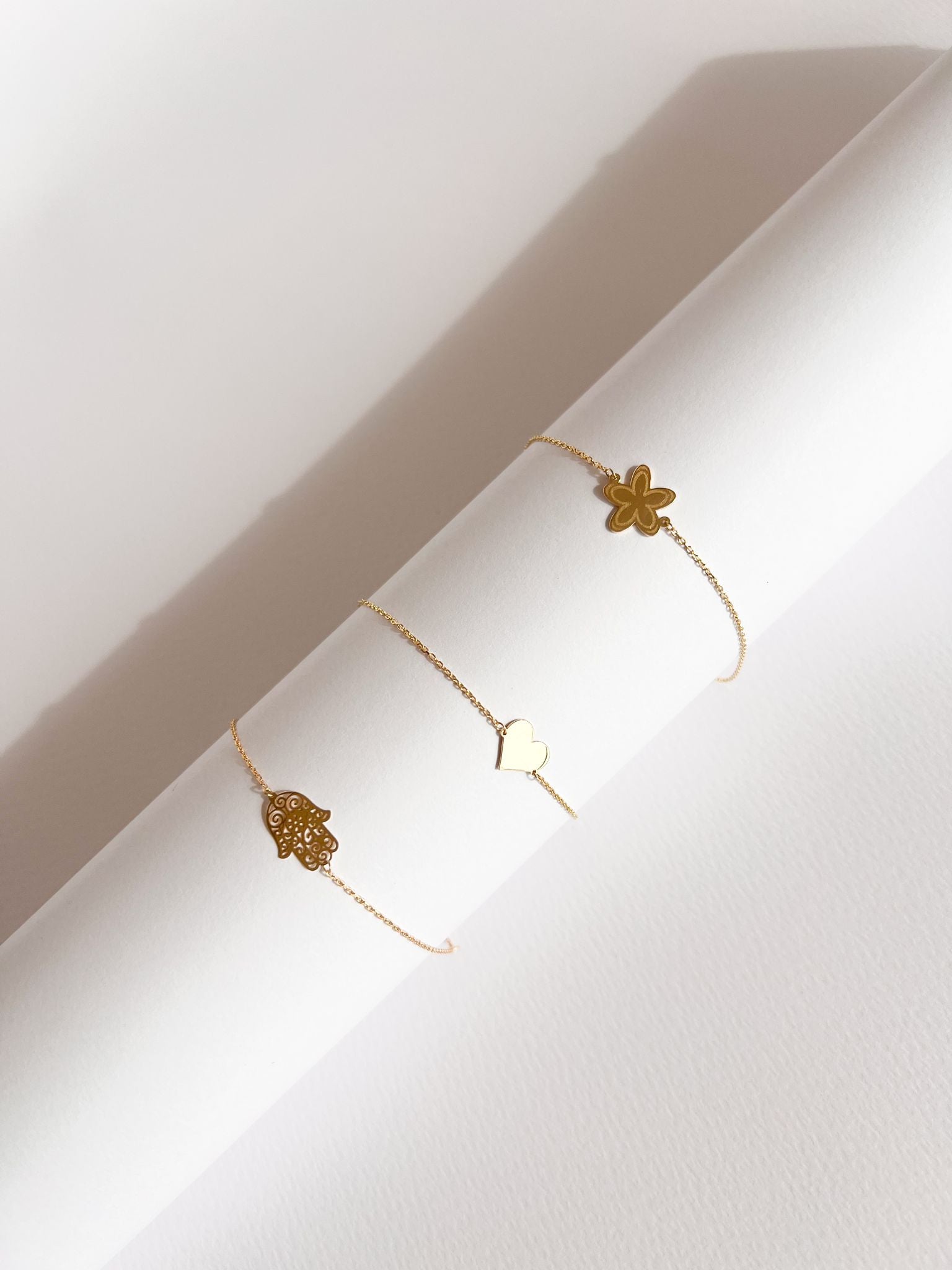 Enti Fatima, Jamila, and Warda bracelets, handmade in 18k gold with hamsa, heart, and flower designs, displayed on white background
