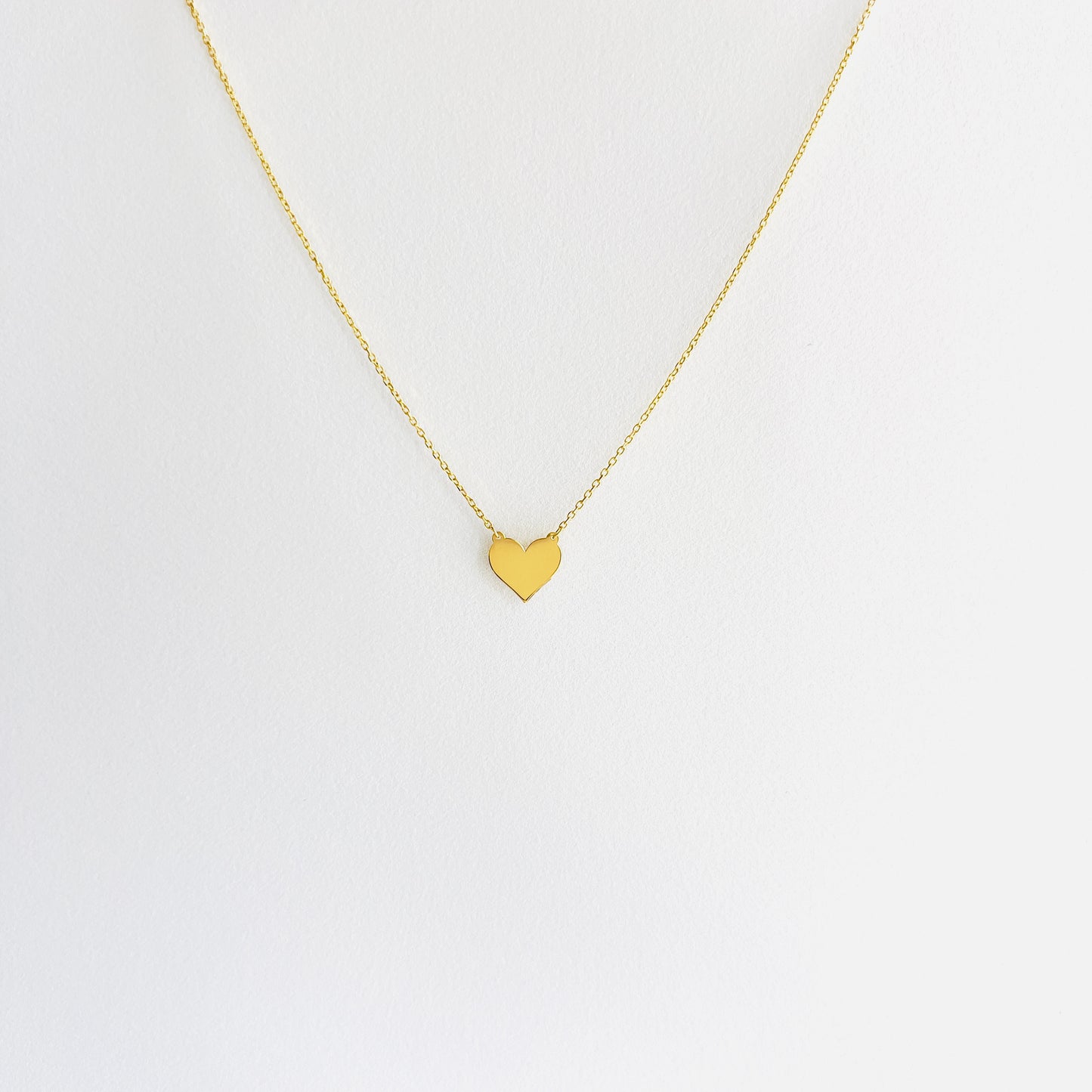 Enti Jamila necklace, handmade in 18k gold with a delicate heart charm and gold chain, displayed on white background
