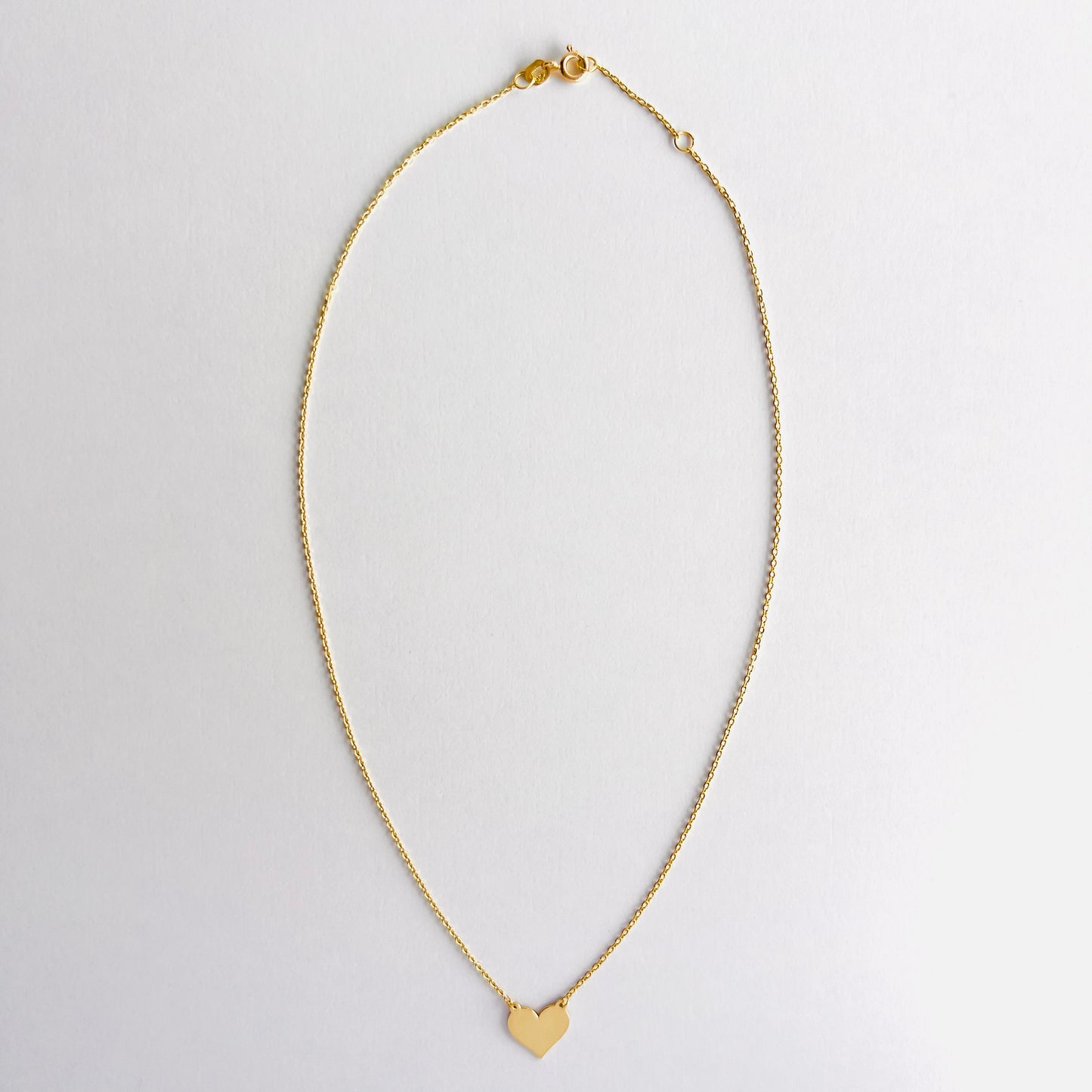 Enti Jamila necklace, handmade in 18k gold with a delicate heart charm and gold chain, displayed on white background