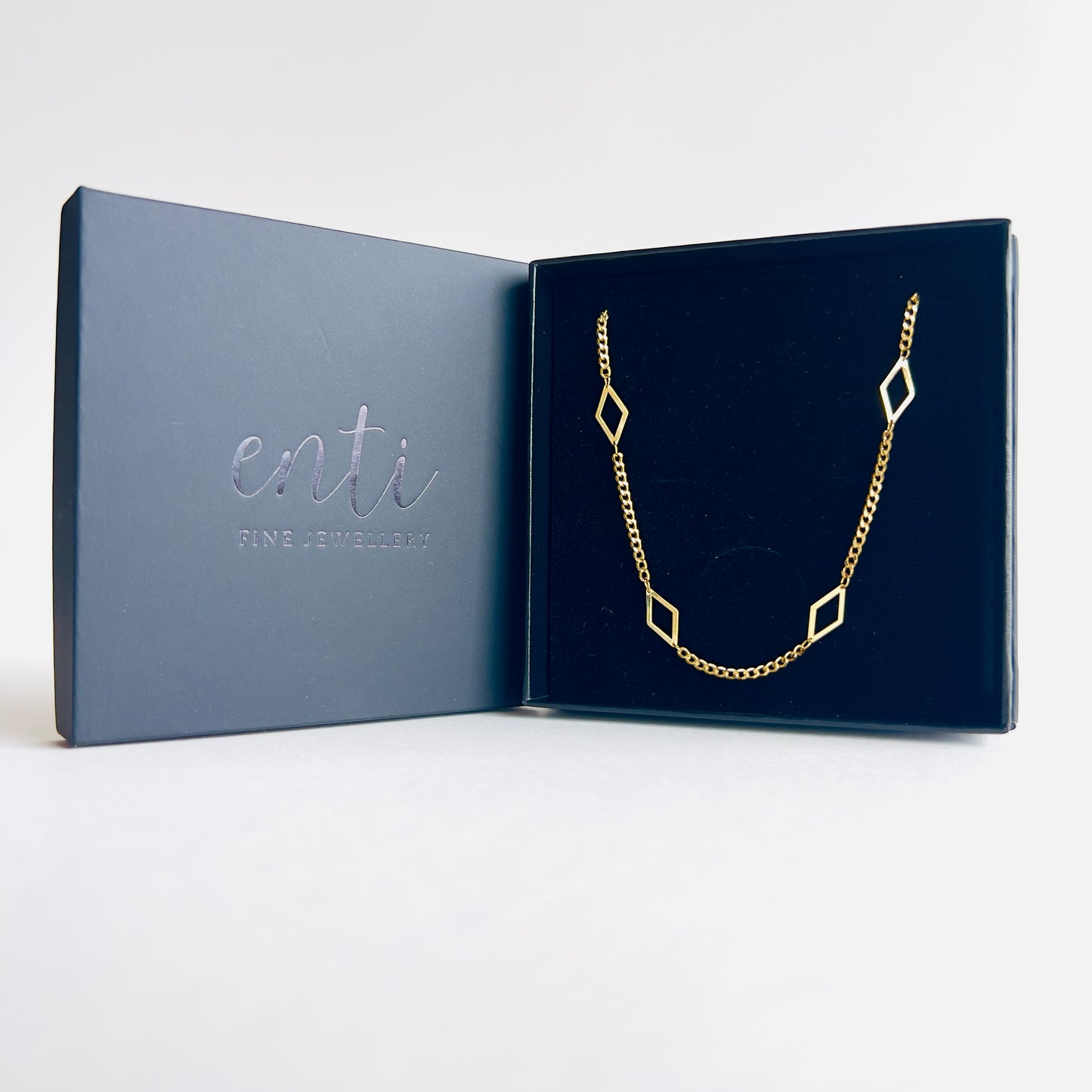 Enti Leila necklace, handmade in 18k gold with a sleek diamond-shaped geometric pendant and gold chain, presented in the signature Enti Jewellery box