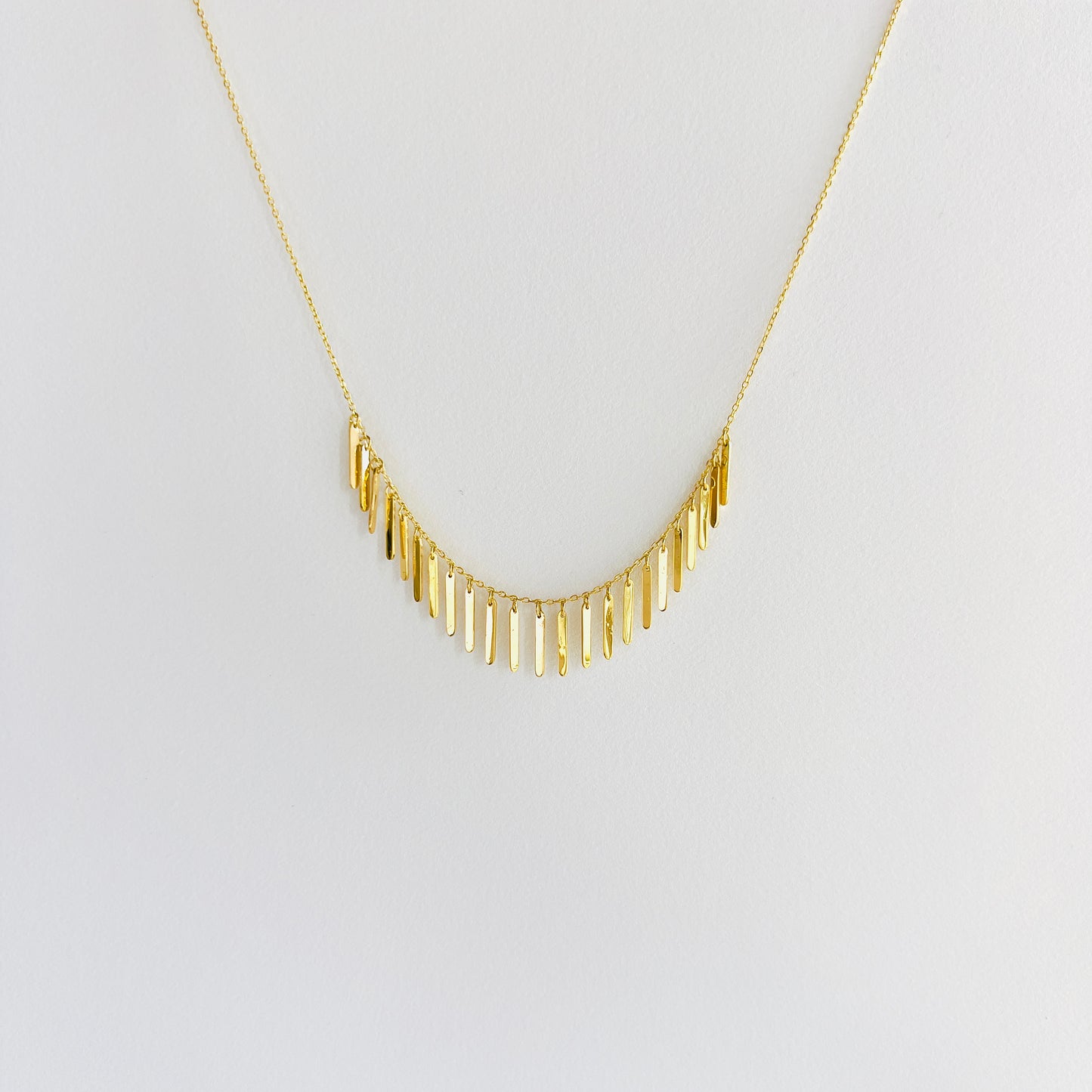 Enti Samira necklace, handmade in 18k gold with small light-catching pendants and gold chain, displayed on white background