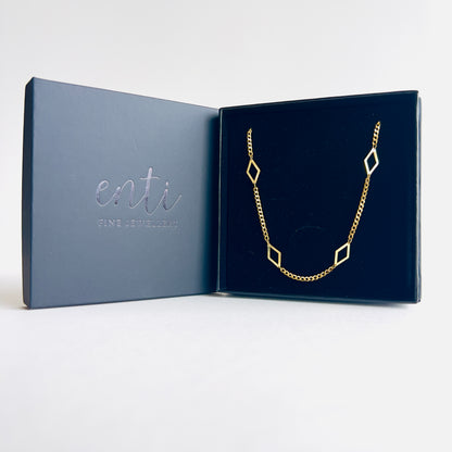 Enti Leila necklace, handmade in 18k gold with a sleek diamond-shaped geometric pendant and gold chain, presented in the signature Enti Jewellery box