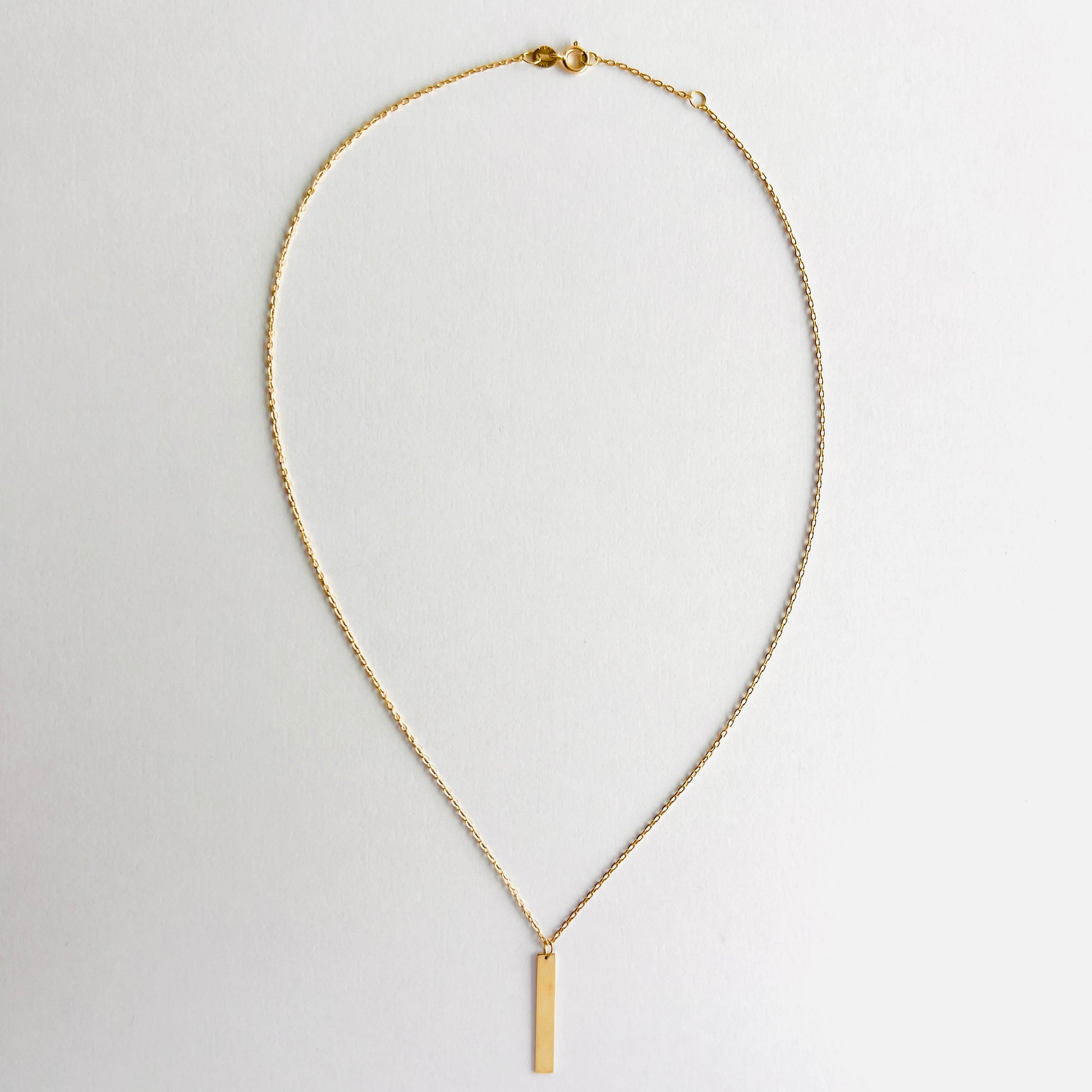 Enti Zara necklace, handmade in 18k gold with a sleek bar pendant and gold chain, displayed on white background
